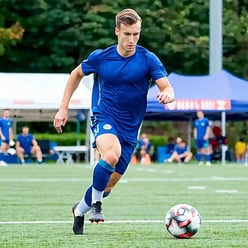 an athletic man playing soccer He should be shown running on a soccer field while kicking a soccer ball during a match