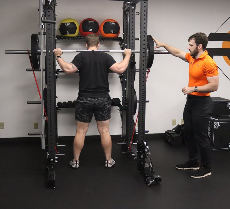 Physical therapist guiding barbell squat technique at Rock Solid